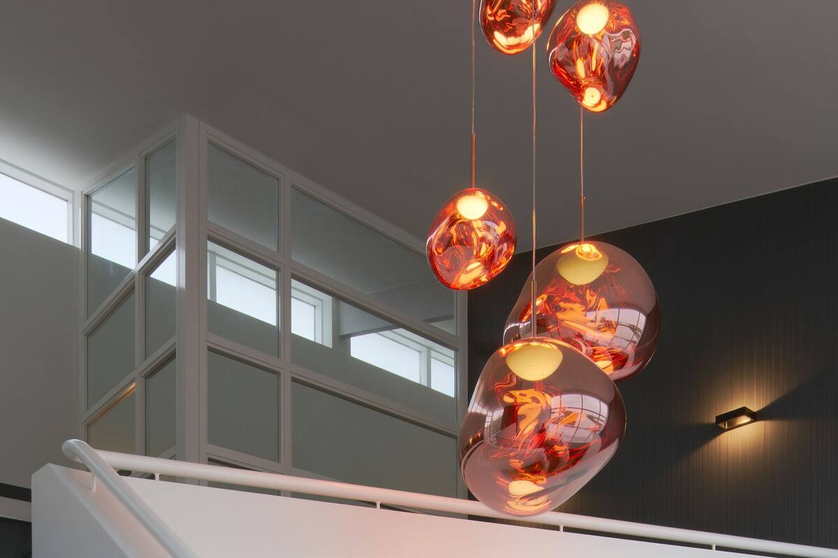 A modern staircase with a white handrail and glass railings, leading to a second floor with large windows and a dark wall.