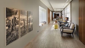 Un hall d’entrée spacieux avec un long plancher en bois, un coin salon doté de canapés et d’une table basse, et de grandes fenêtres laissant entrer la lumière naturelle.