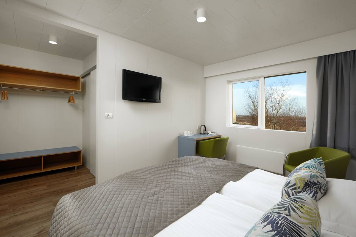 A hotel room with a bed, a desk, a chair, a TV, and a window with a view.