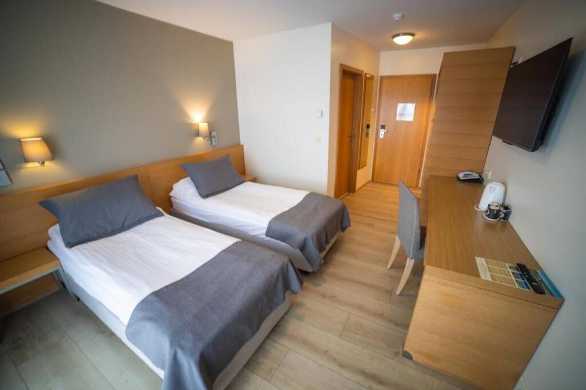 Habitación de hotel con dos camas individuales, un escritorio con silla, televisión de pantalla plana y armario de madera.