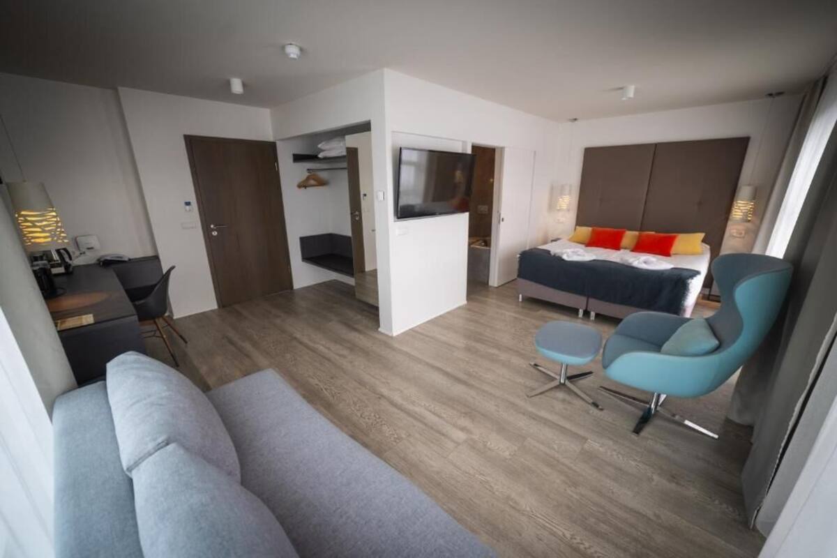 Habitación de hotel moderna con sofá, cama con almohadas rojas y amarillas, televisión y escritorio con silla.