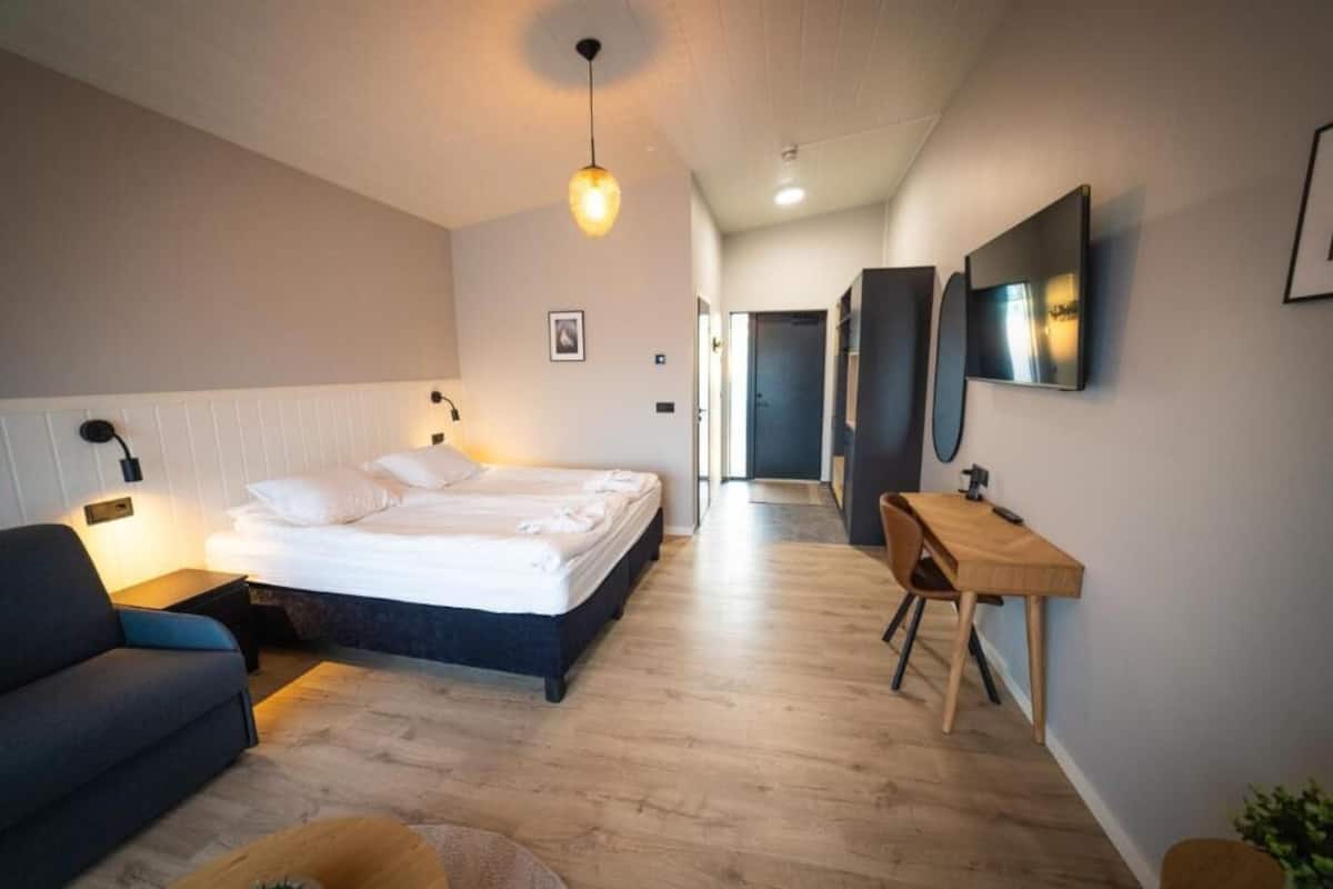 A modern hotel room with a bed, bedside table, and a desk with a chair.