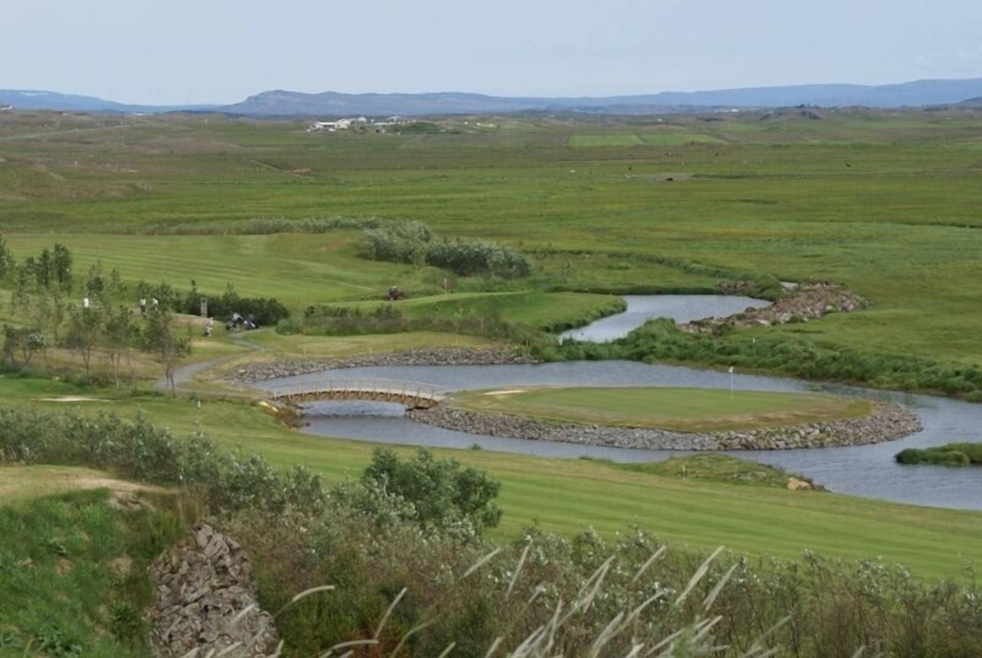 A golf course with a river running through it, surrounded by green fields and distant hills.