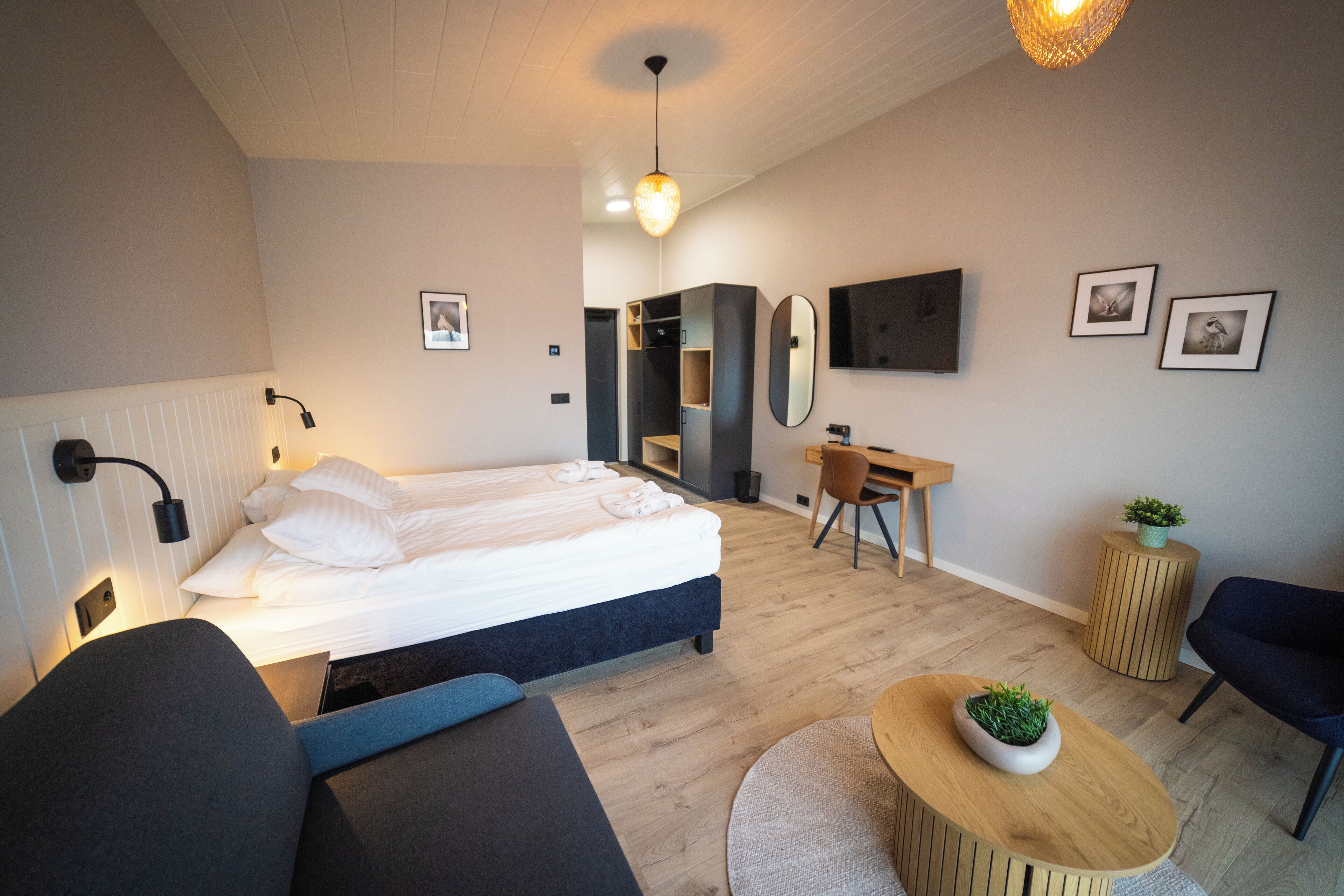 Una habitación de hotel moderna con una cama, un escritorio, una silla, una mesa redonda de madera y una pequeña planta en maceta.