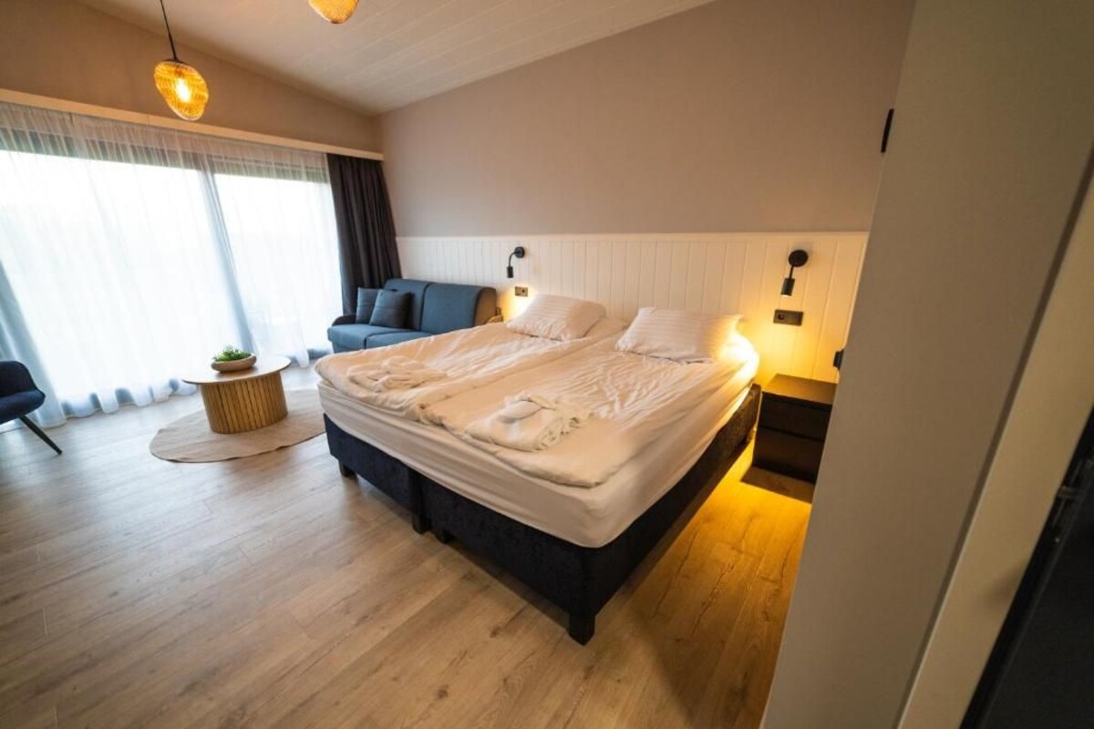 Un dormitorio moderno con una cama grande, un sofá, una pequeña mesa redonda y una ventana con cortinas.