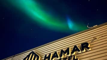 The exterior of the Hamar Hotel with a view of the Northern Lights in the background.