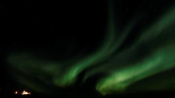 The Northern Lights over a dark landscape with distant lights in the background.