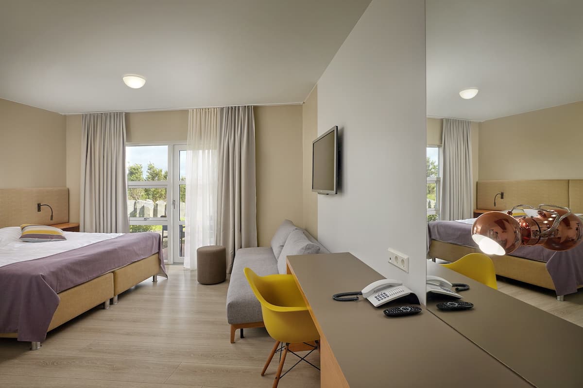 A hotel room with two beds, a desk, a chair, a television, and a view of the outdoors.