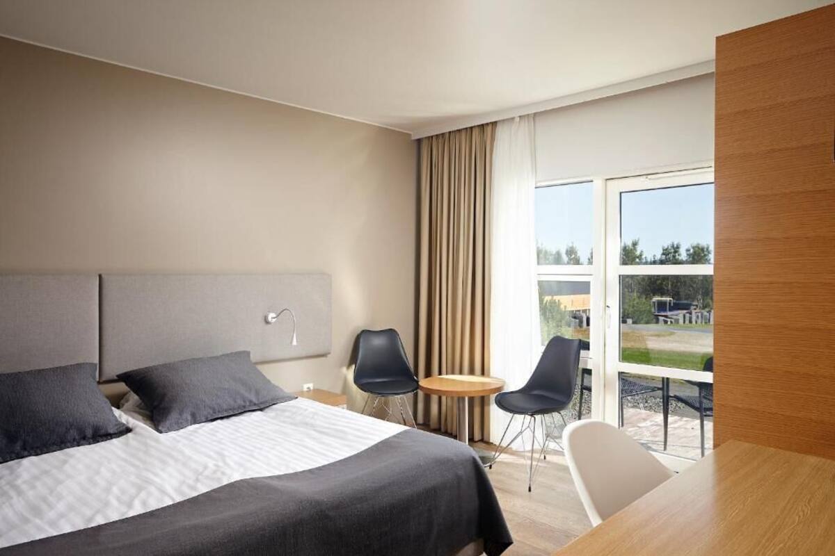 Una habitación de hotel moderna con una cama grande, dos sillones, una mesita y vistas al exterior.