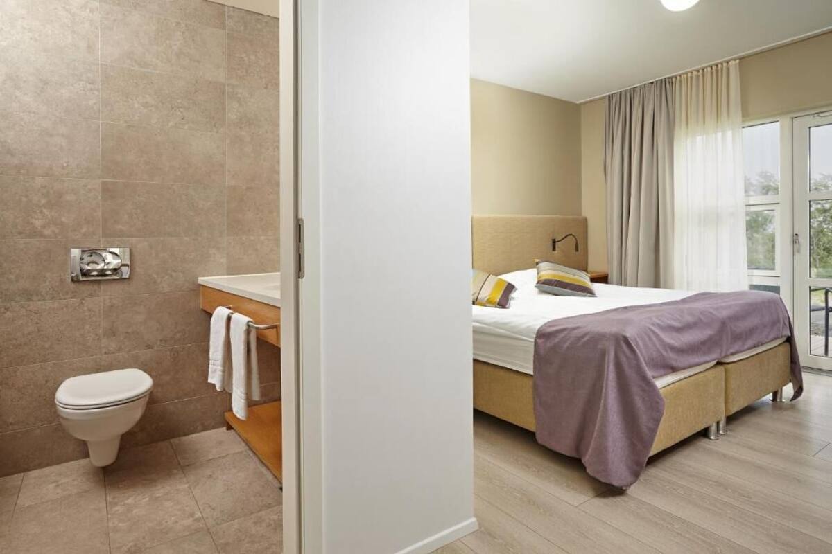 Una habitación de hotel con baño, una cama con una manta morada y vistas al exterior.
