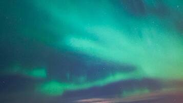Un estacionamiento con un edificio al fondo y un cielo nocturno con auroras verdes.