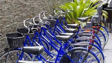 A row of blue bicycles parked against a stone wall, with a potted plant in the background.