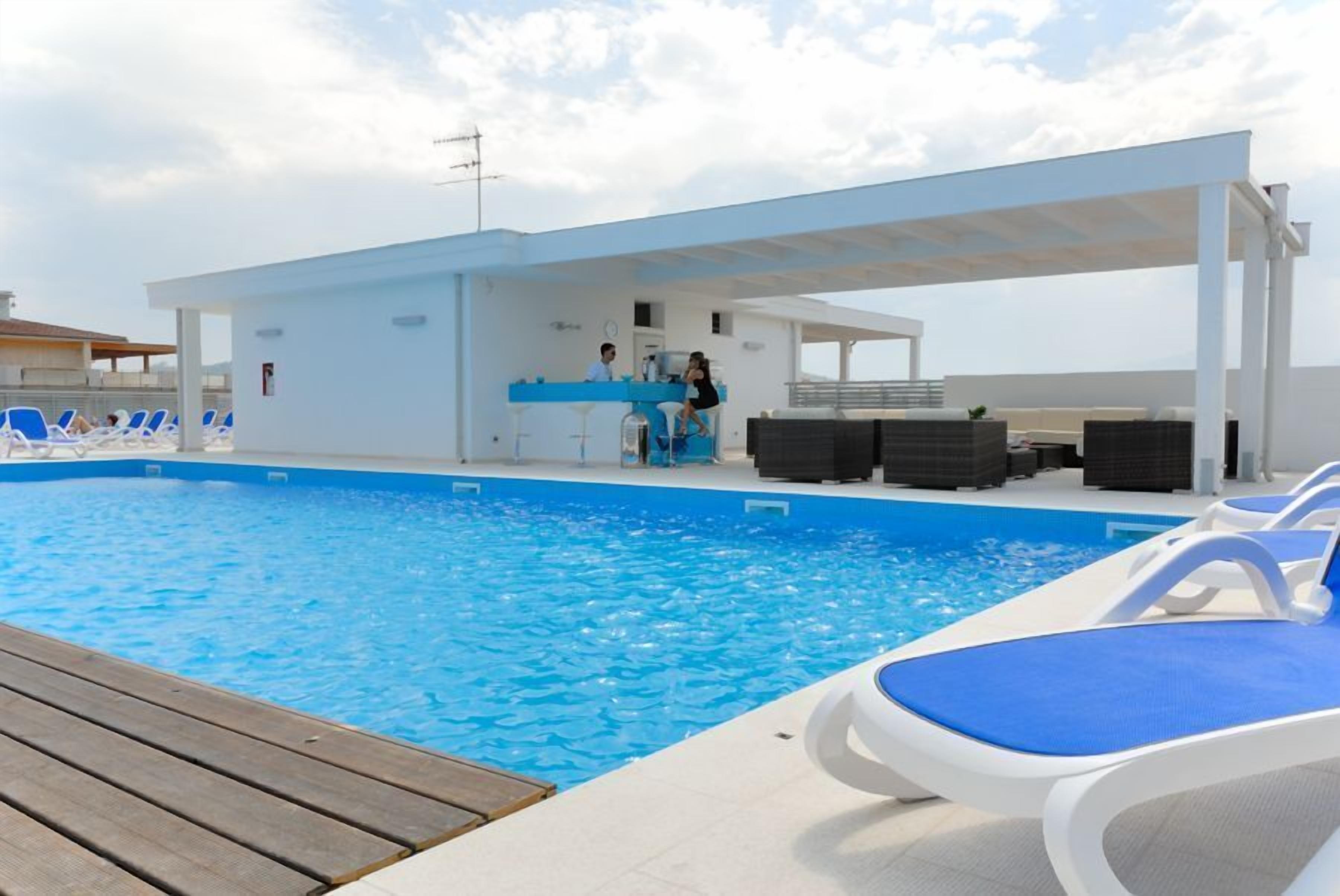 Zona de piscina con sillones de descanso, un bar y un espacio de estar cubierto.