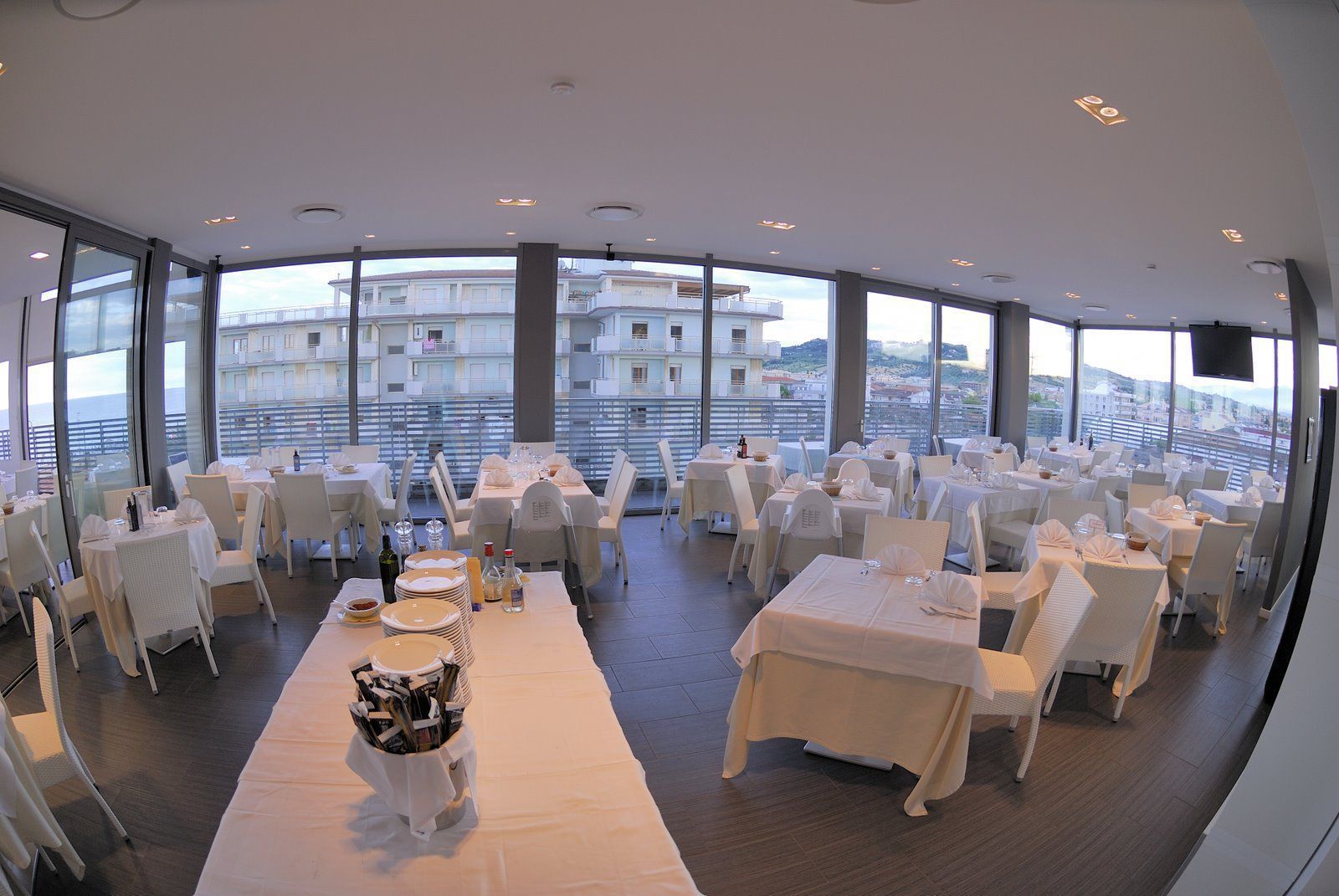 A restaurant with white tables and chairs, large windows, and a view of buildings.