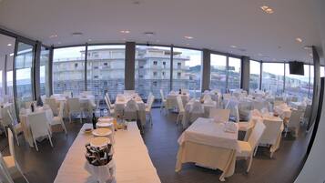 A restaurant with white tables and chairs, large windows, and a view of buildings.