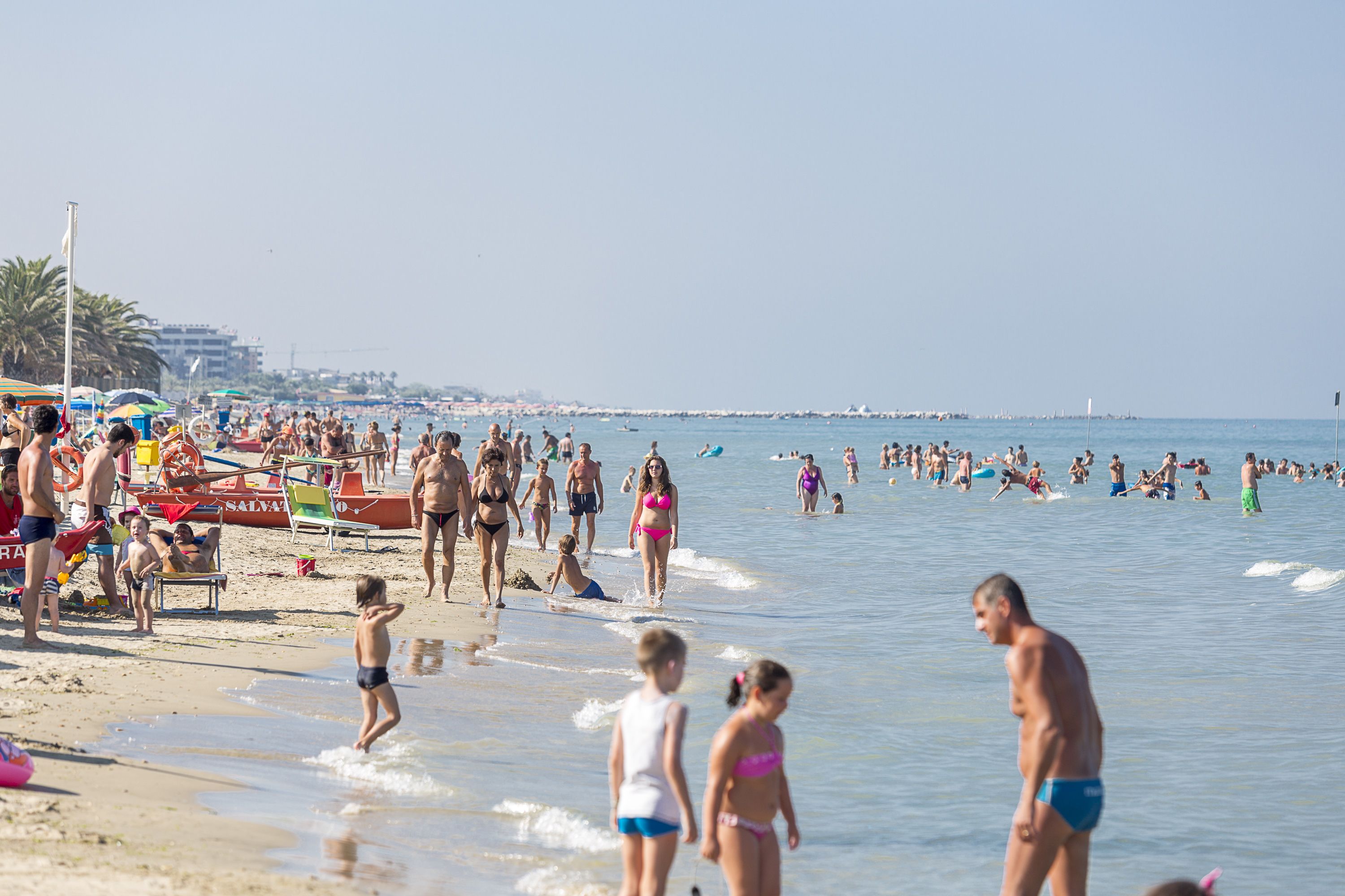 Una playa concurrida, gente en trajes de baño, sombrillas y sillas de playa.