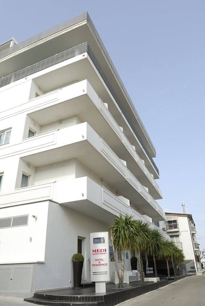 Un hotel de varios pisos con balcones, un letrero que indica que es un hotel complejo jardín, y un cielo despejado.