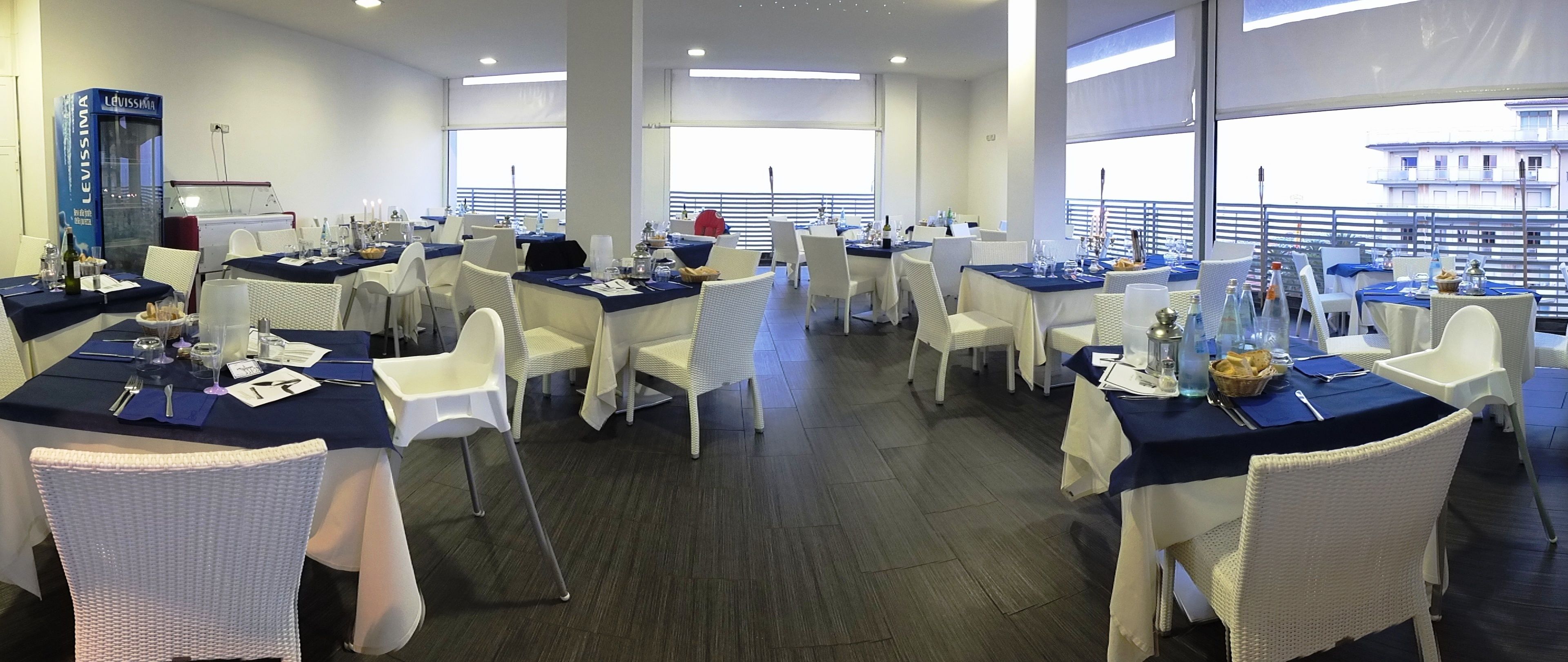 A spacious dining area with multiple tables set for guests, featuring white wicker chairs and dark blue tablecloths.