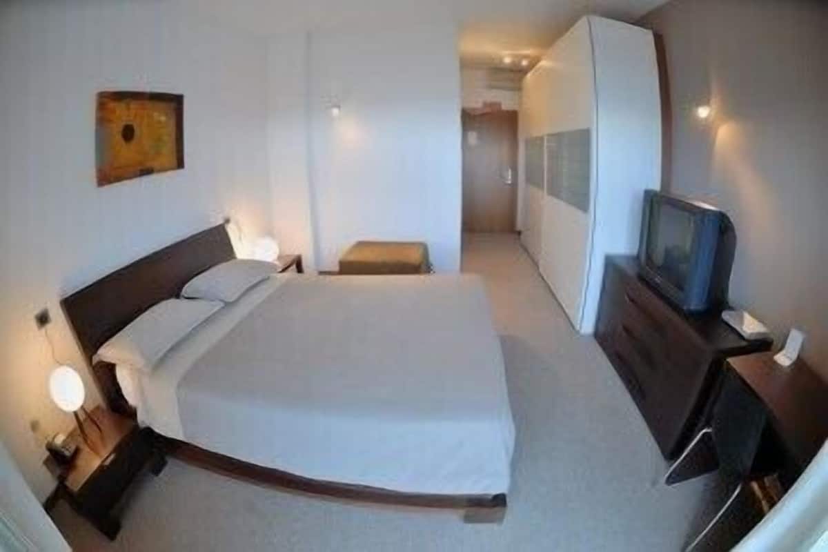 A hotel room with a bed, bedside table, lamp, wardrobe, and a television.