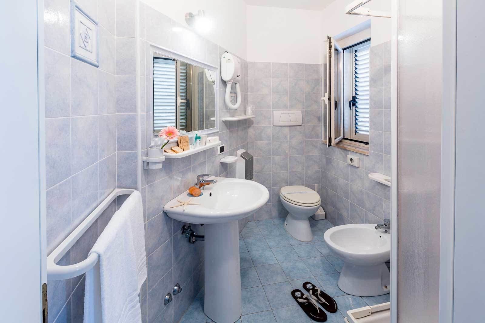 Un baño con lavabo, inodoro, bidé y ventana con persianas.