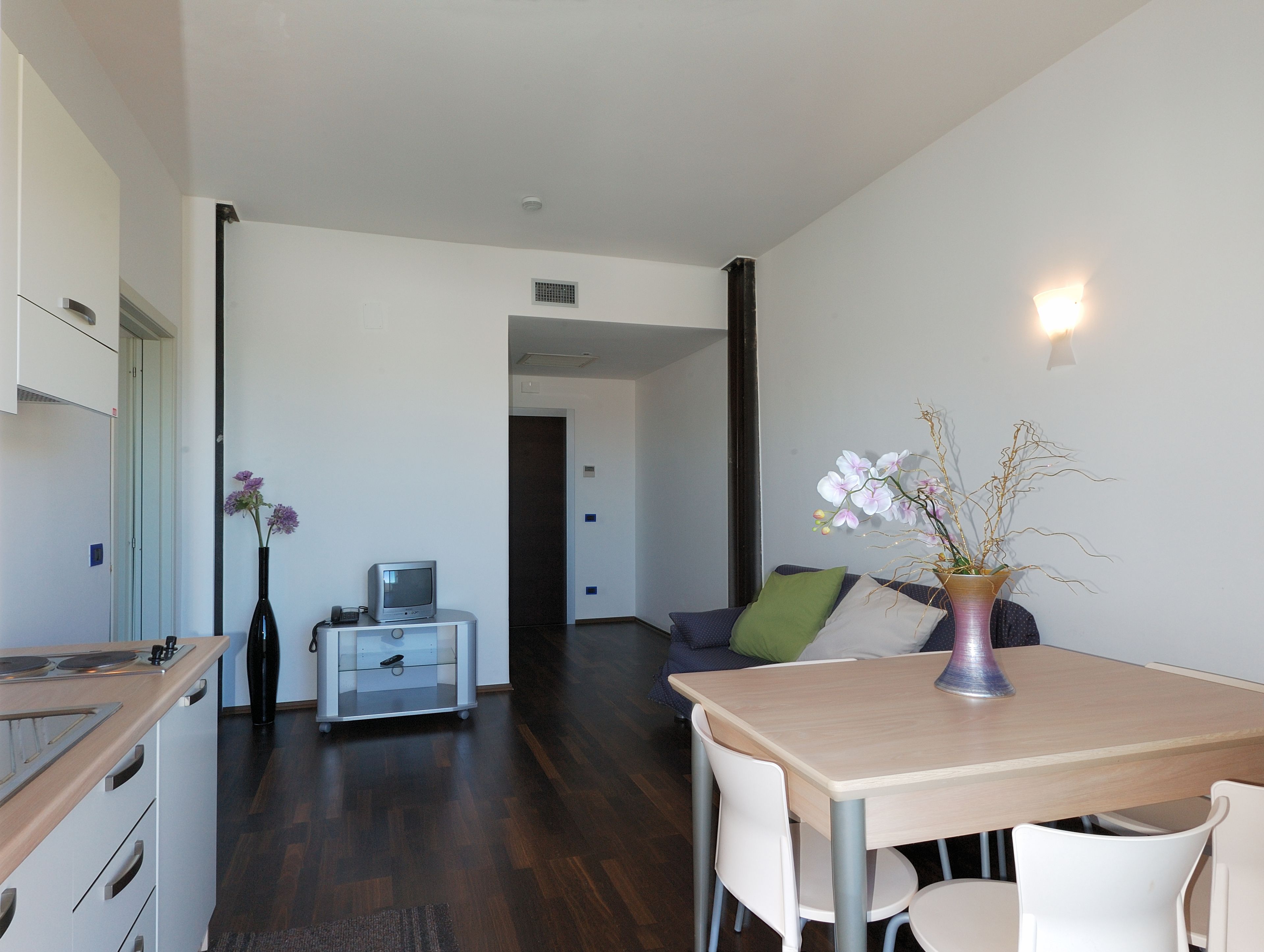 Una cocina moderna con comedor, un televisor pequeño y un jarrón con flores.
