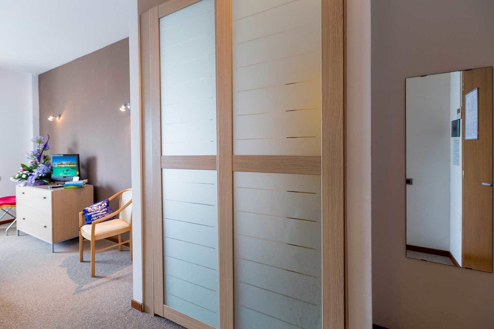 Une chambre d’hôtel avec une porte coulissante, un bureau avec un ordinateur et des fleurs, une chaise et un miroir.