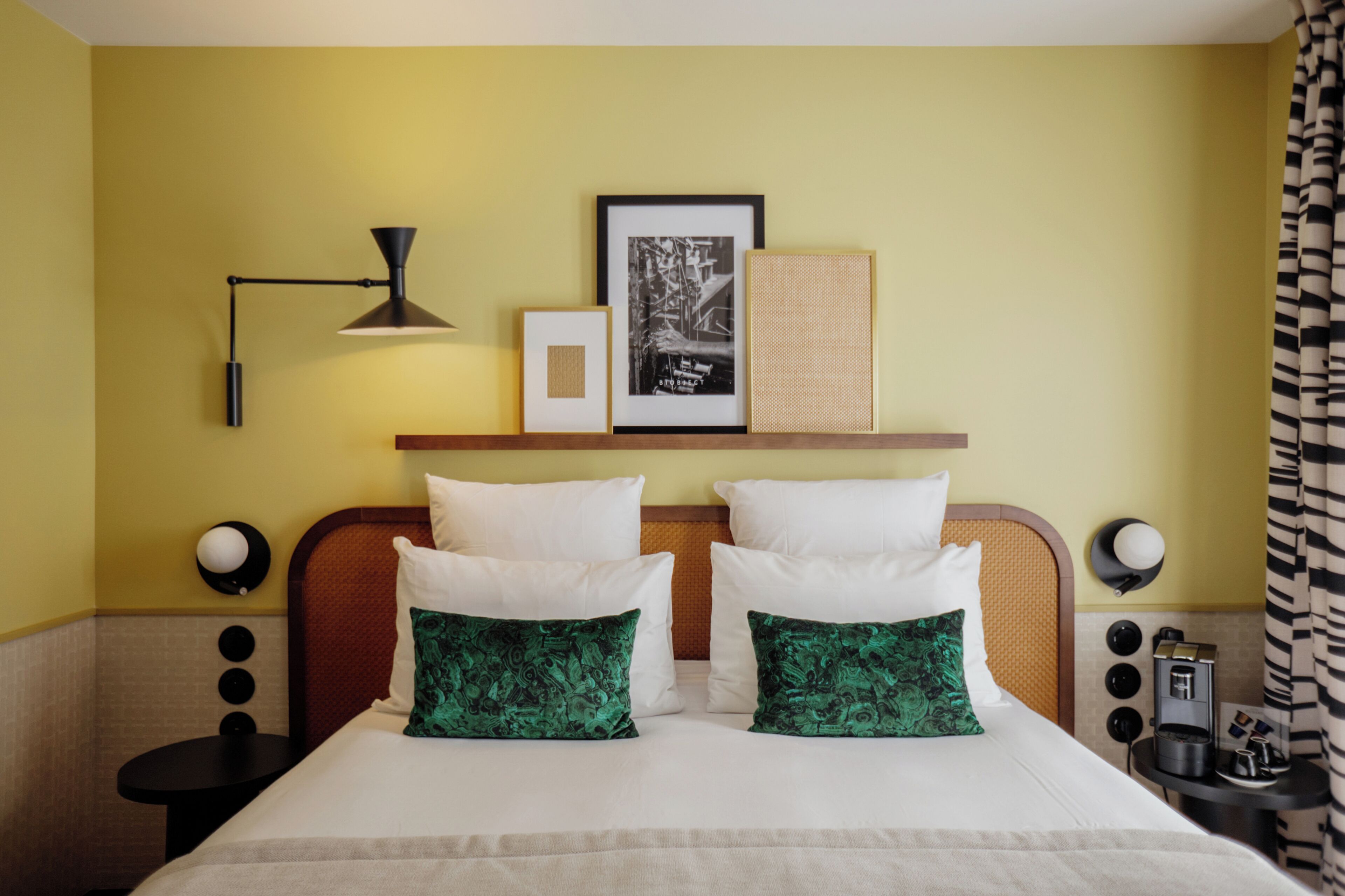 A hotel room with a bed, bedside tables, a lamp, a framed picture, and a shelf with a woven basket.