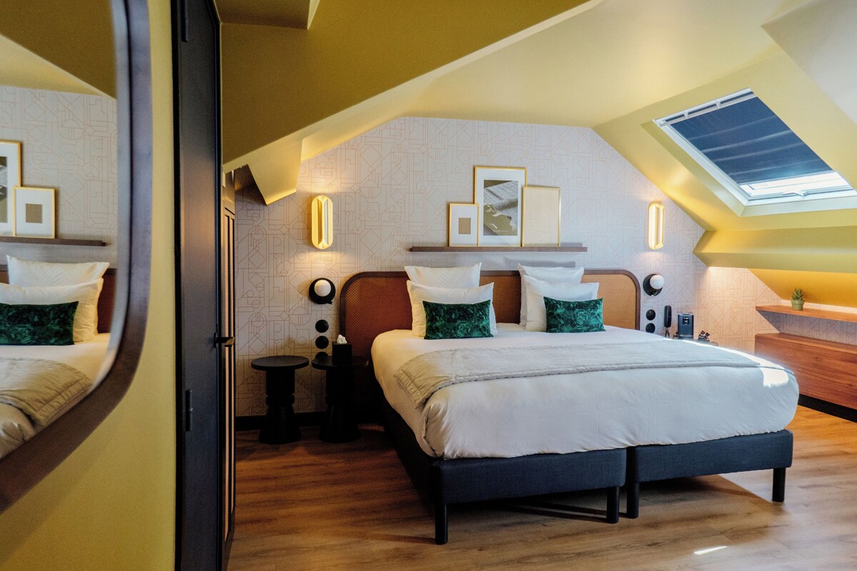 Un dormitorio moderno con un tragaluz, una cama grande con muchas almohadas, una mesita de noche y un espejo.