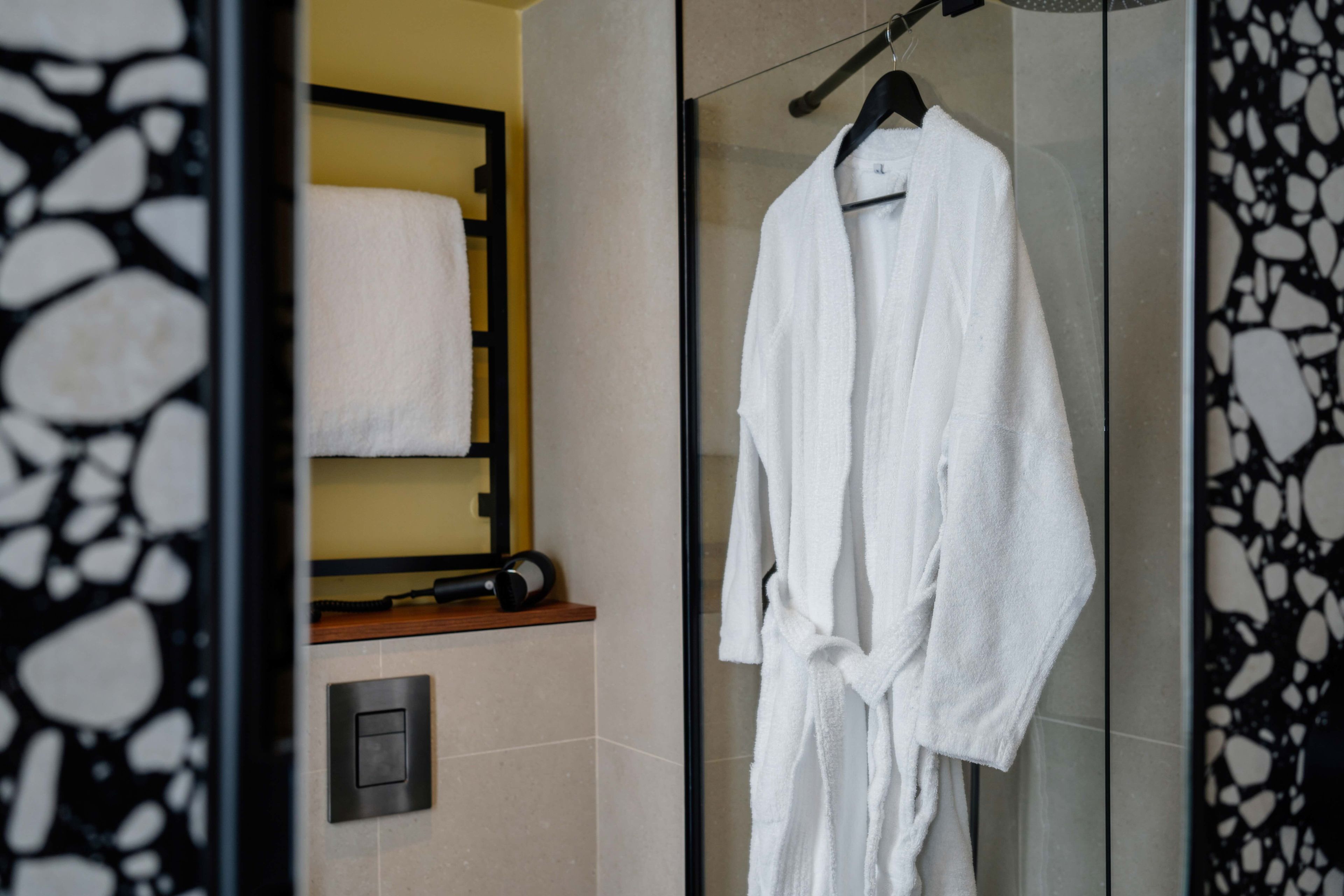 Un baño con cabina de ducha de vidrio, un albornoz blanco colgado en un perchero y una toalla en un estante.
