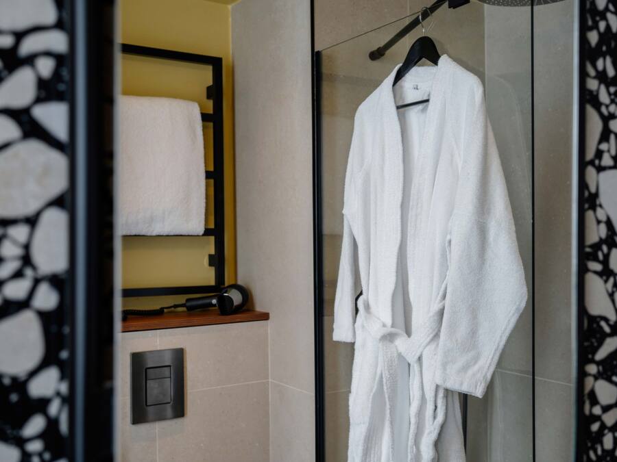 Un baño con cabina de ducha de vidrio, un albornoz blanco colgado en un perchero y una toalla en un estante.