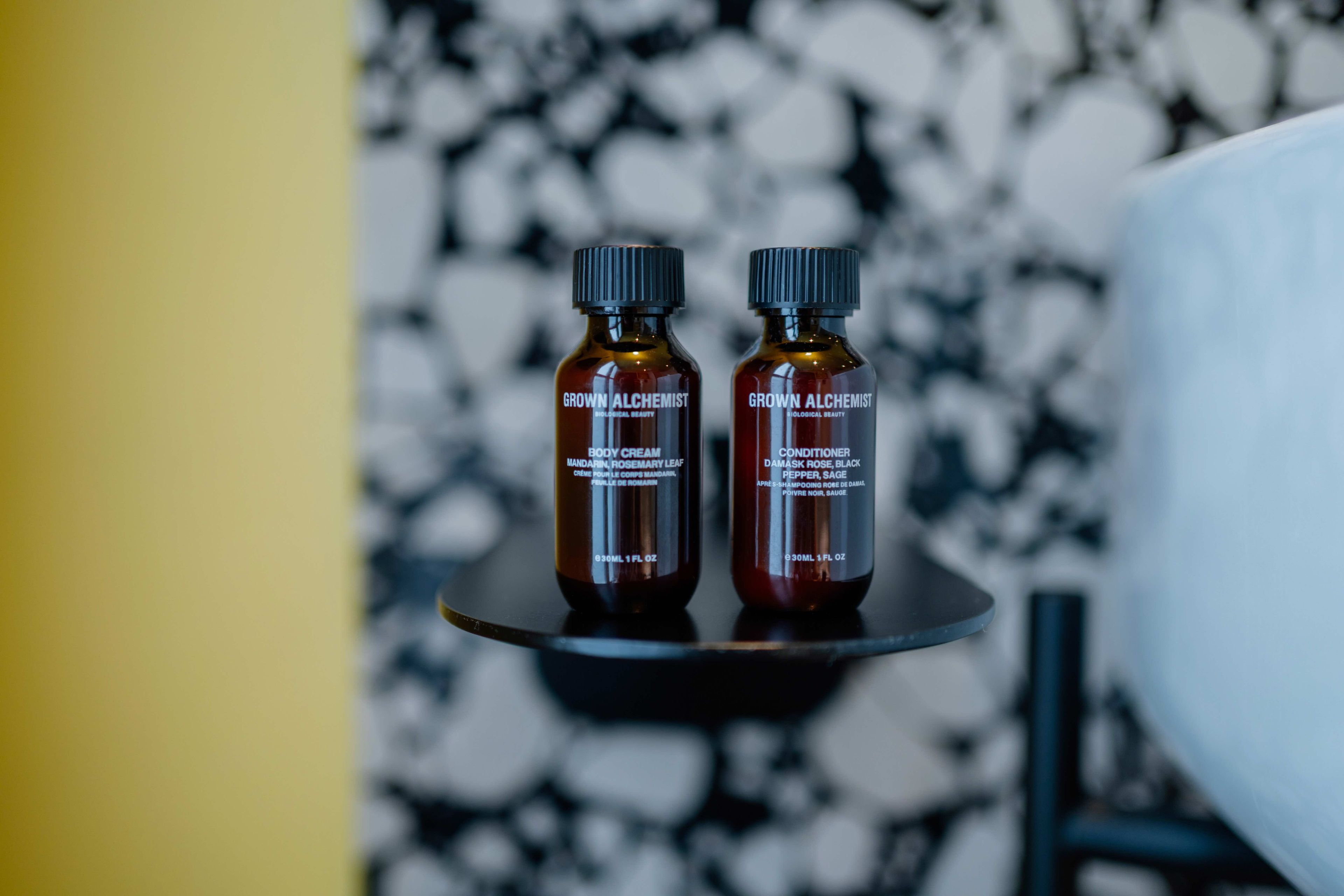 Dos botellas de productos 'Grown Alchemist' sobre una bandeja negra frente a una pared de mármol.