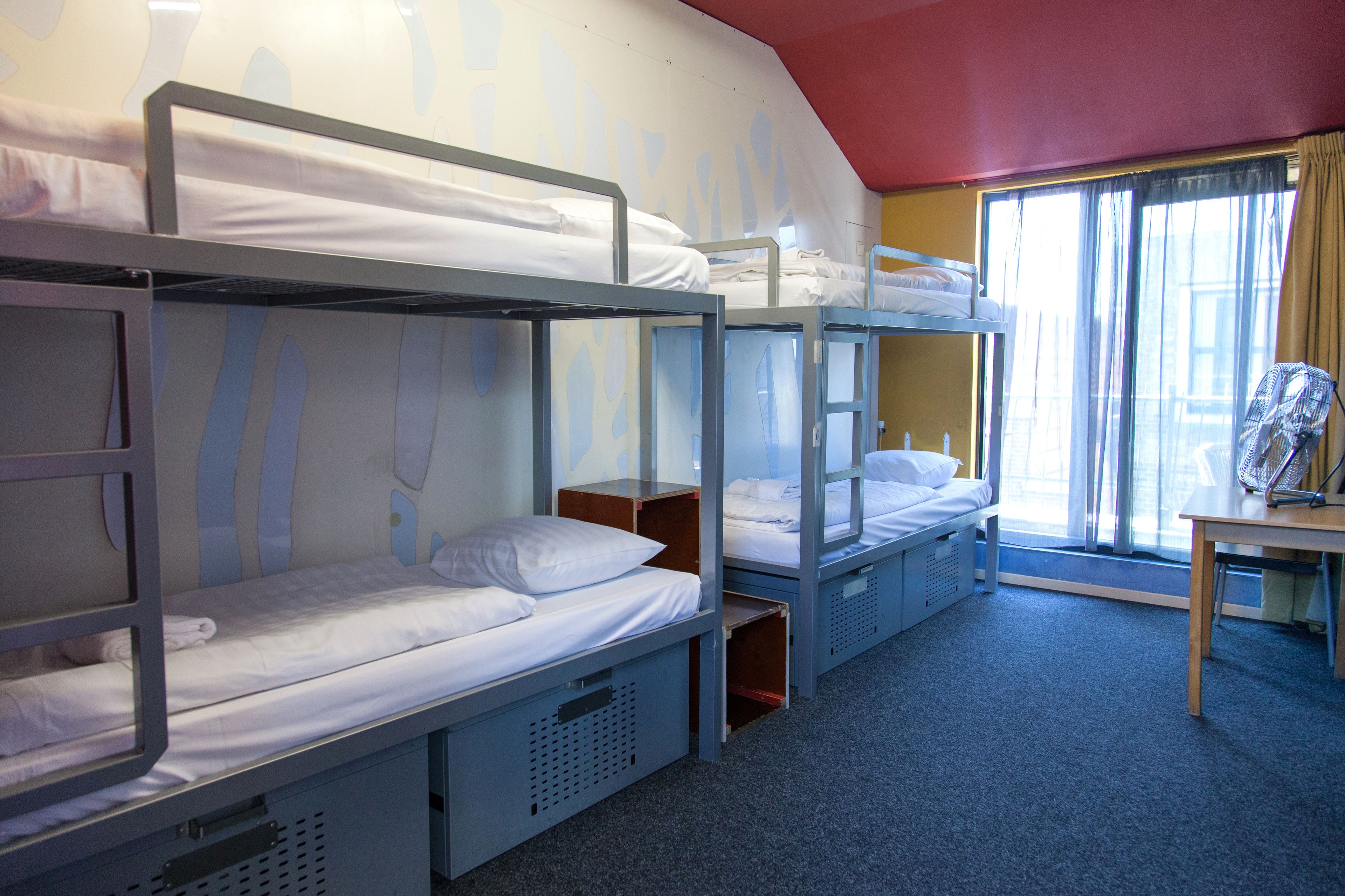Une chambre de dortoir avec des lits superposés, une fenêtre avec des rideaux et une petite table avec une chaise.
