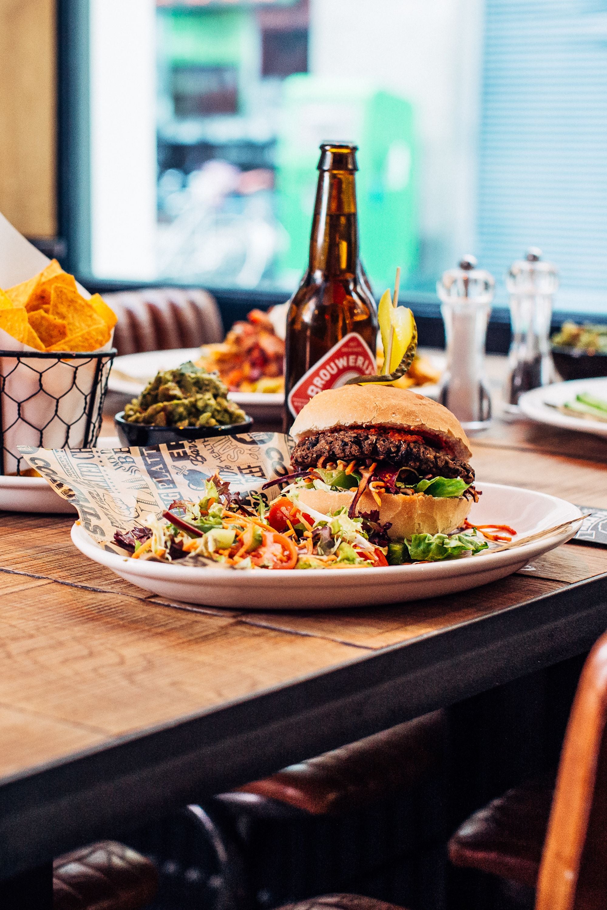 A restaurant setting with a burger, guacamole, and a beer bottle on the table.