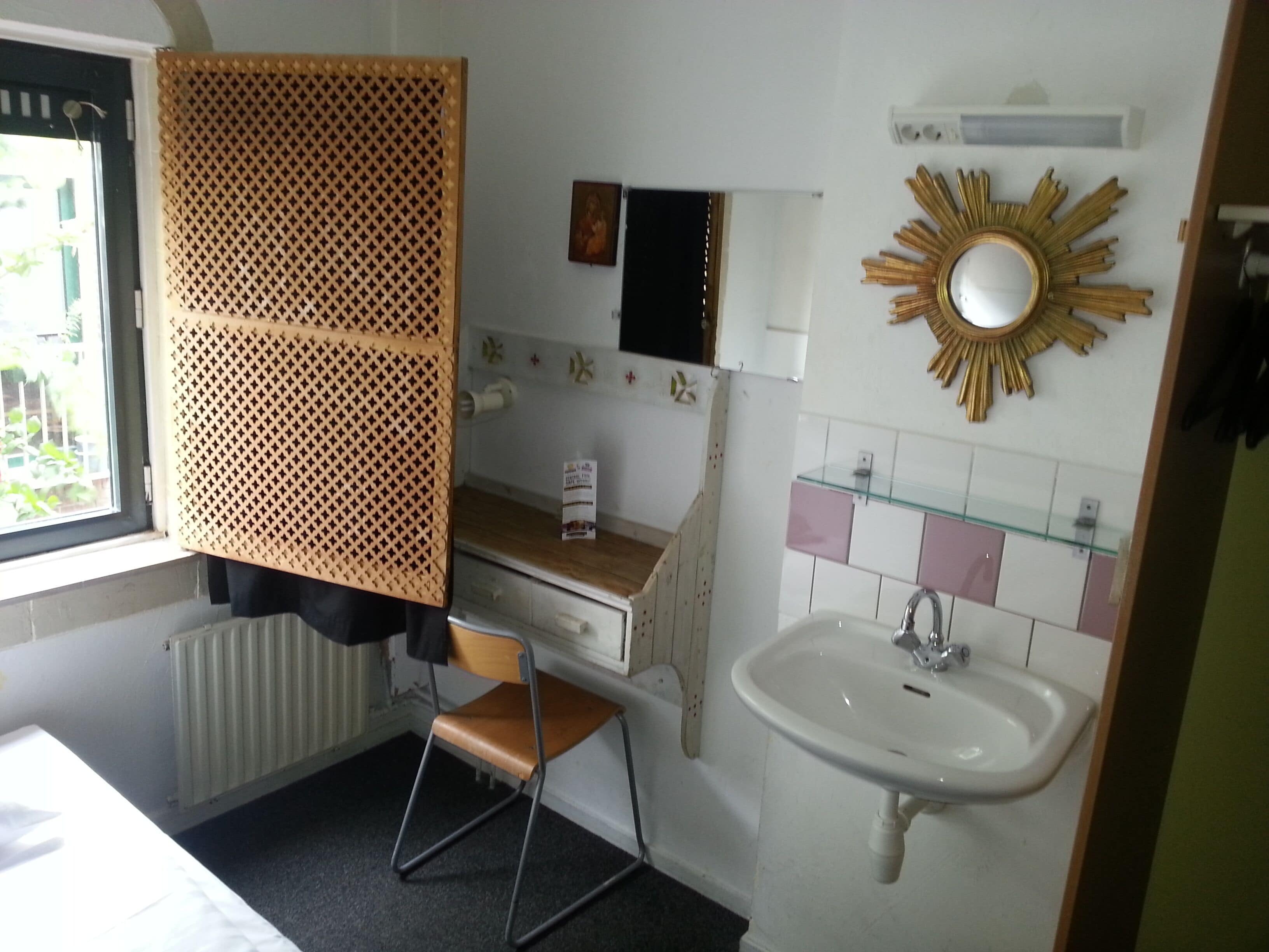 A compact bathroom with a sink, mirror, and a window with a view of greenery.