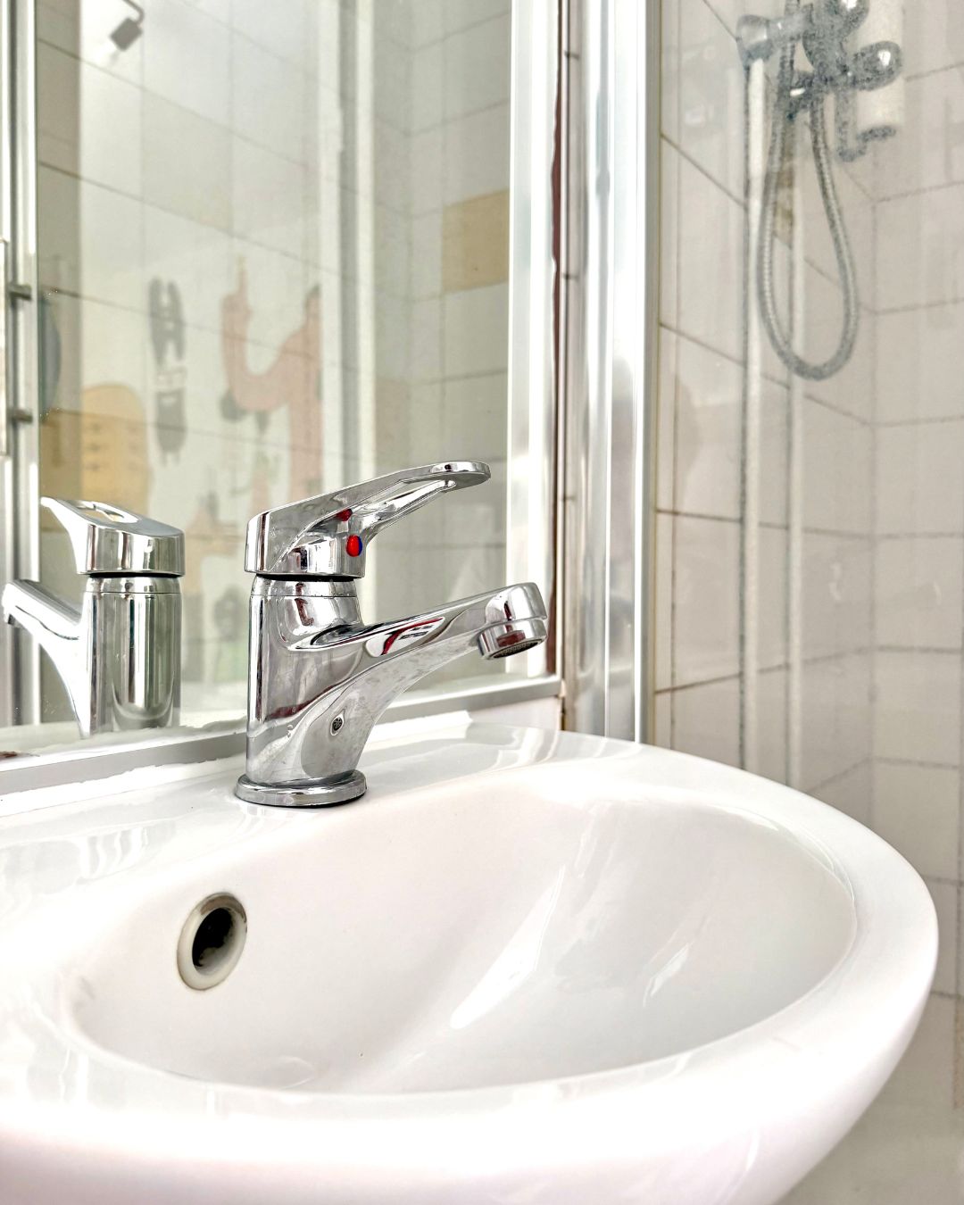 Un baño con lavamanos blanco, grifo cromado y cabina de ducha de vidrio.