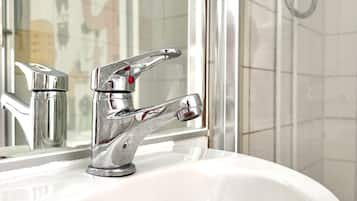 Un baño con lavamanos blanco, grifo cromado y cabina de ducha de vidrio.