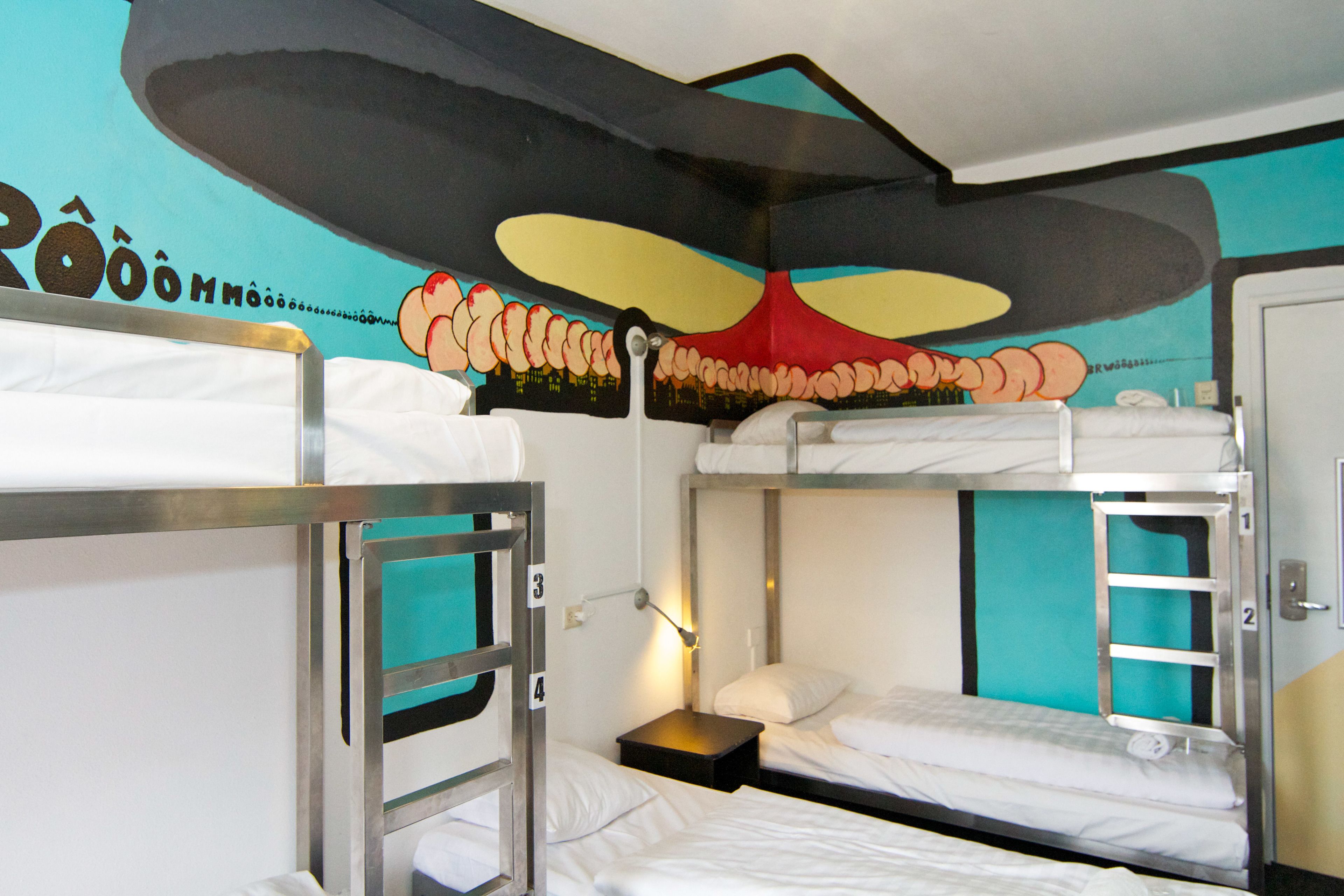 Habitación con literas, un mural en la pared, una mesita de noche y una puerta.