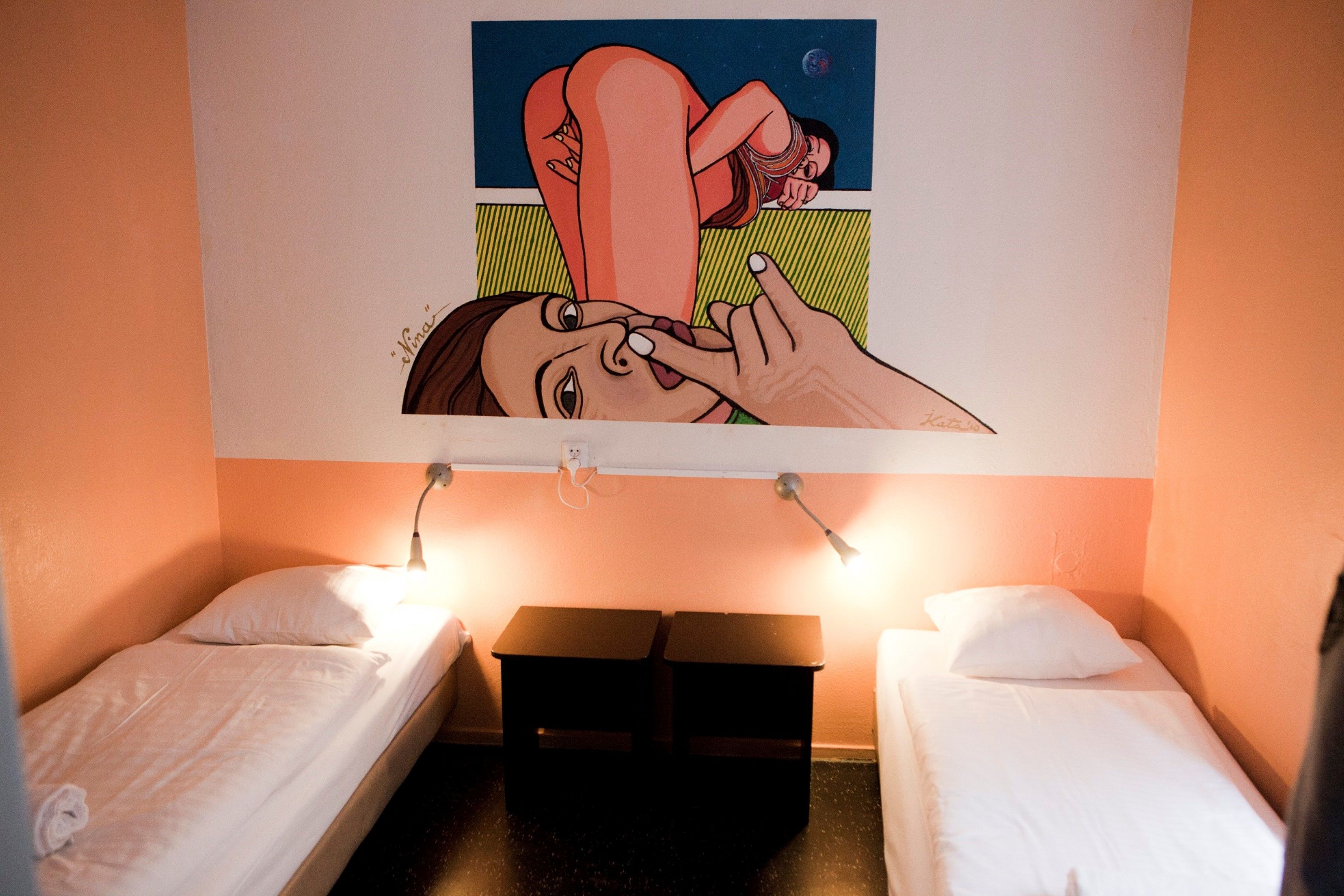 A hotel room with two single beds, a painting above the beds, and a small table between them.