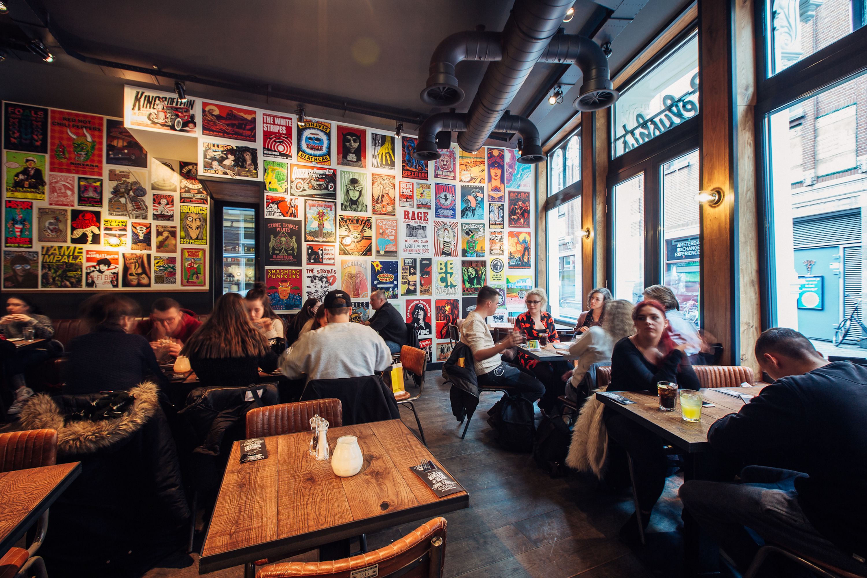 A restaurant with a wall of colorful posters and a view of the street outside.