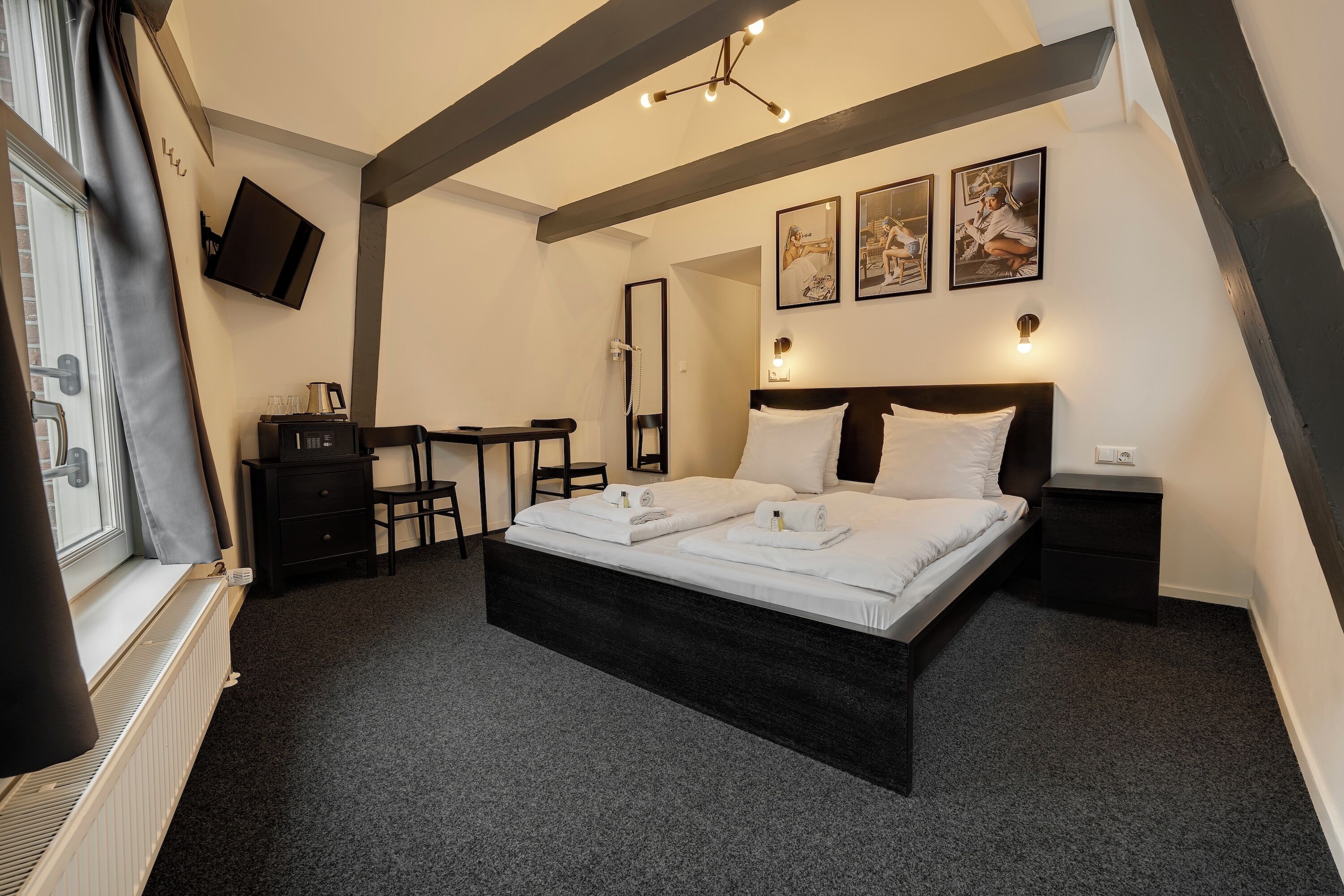 Quarto de hotel moderno com uma cama grande, uma escrivaninha, uma cadeira, televisão de tela plana e obras de arte nas paredes.