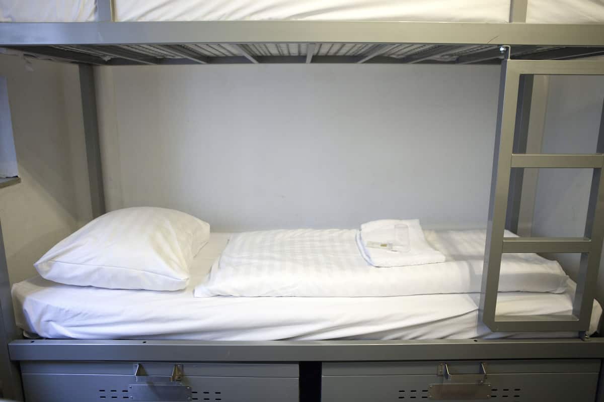 A bunk bed with white bedding and a metal ladder.