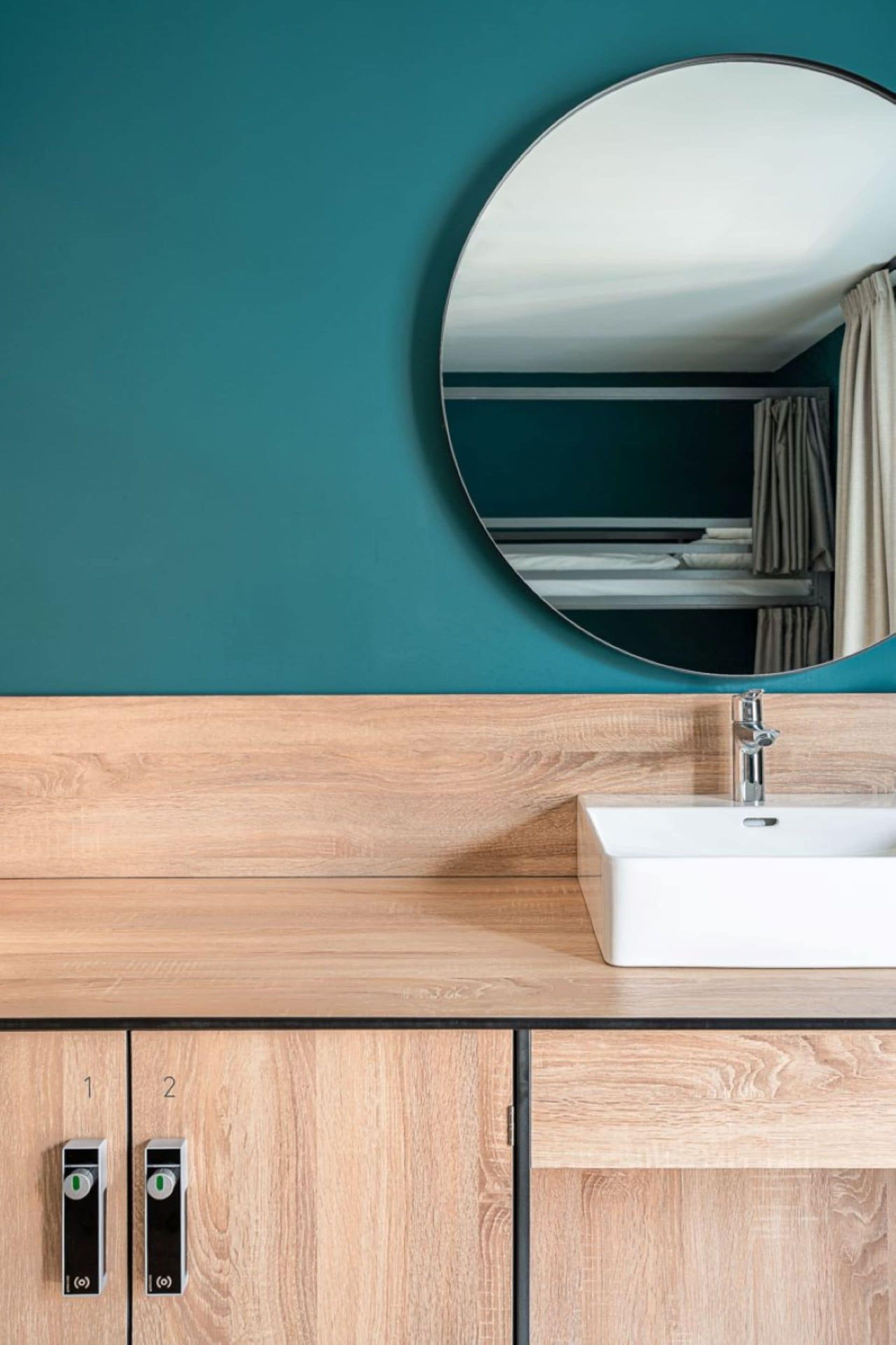 Ein Badezimmer mit einem Holzkosmetikschrank, einem weißen Waschbecken und einem runden Spiegel.
