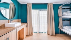 A modern bathroom with teal walls, a wooden vanity, a white sink, and a mirror. - St Christopher's at The Winston - Hostel (Amsterdam)