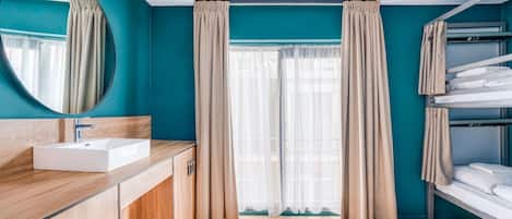 Un baño moderno con paredes color turquesa, un tocador de madera, un lavabo blanco y un espejo.