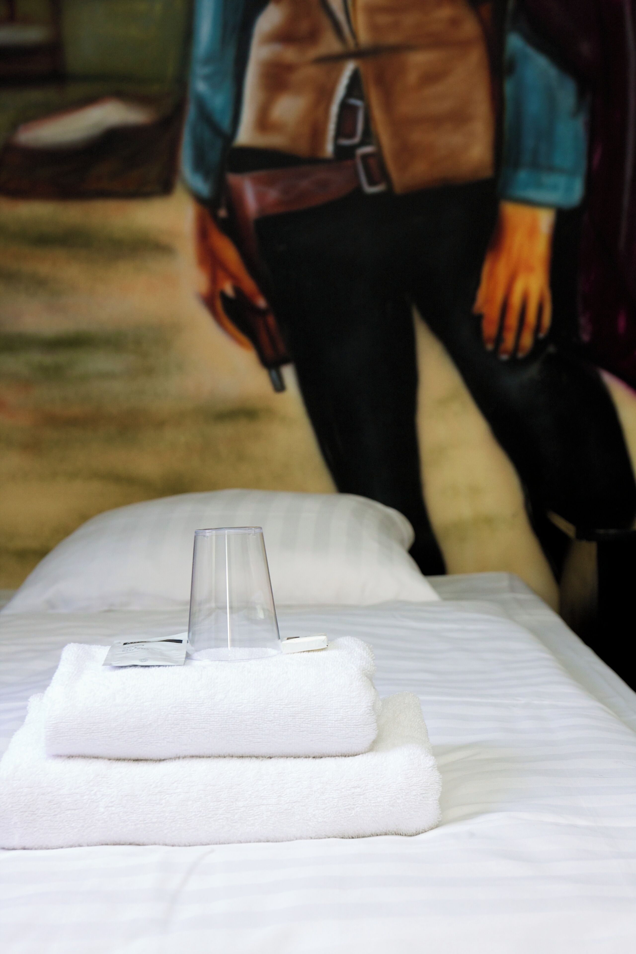 A neatly made bed with a glass of water and folded towels.