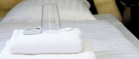 A neatly made bed with a glass of water and folded towels.