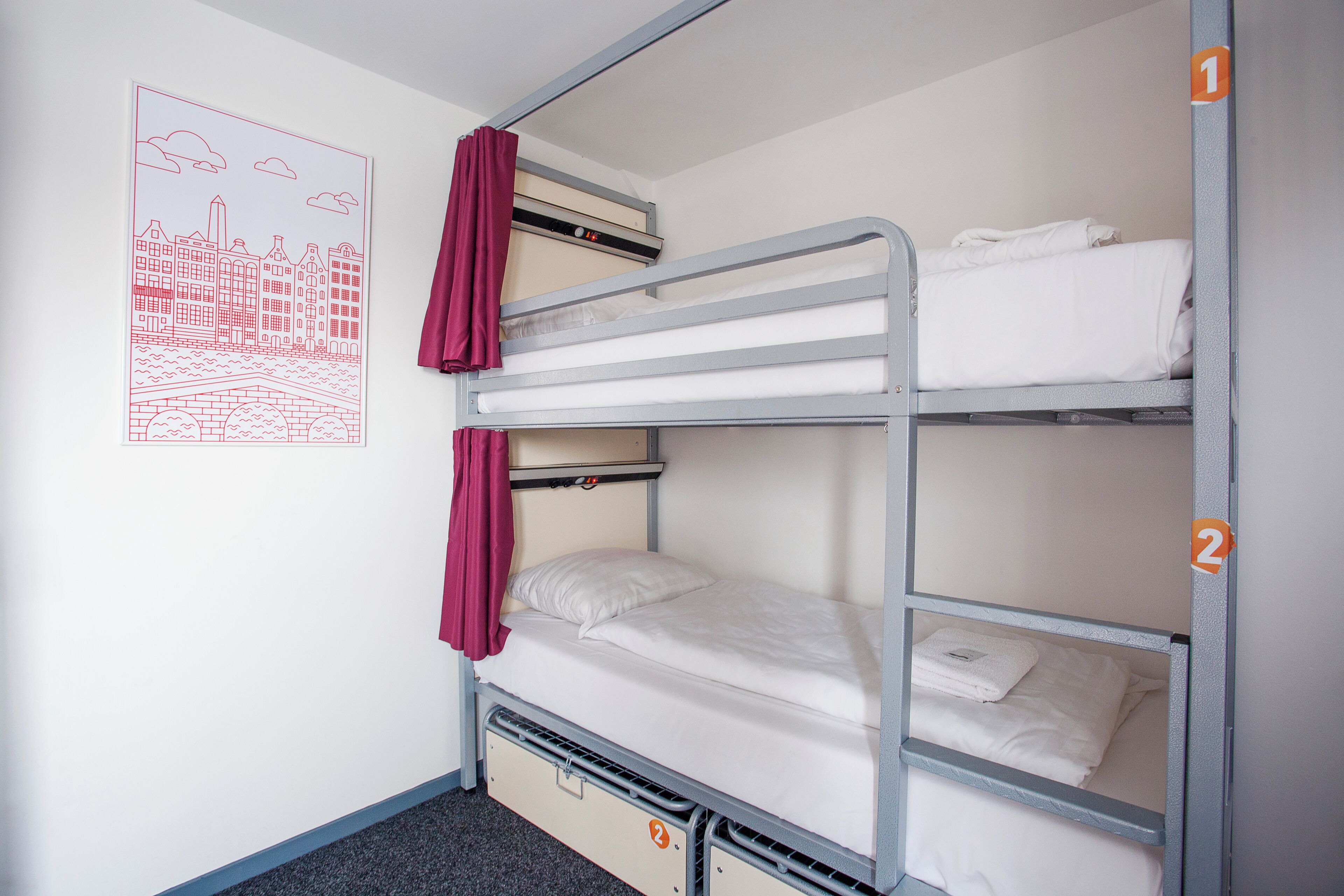 A bunk bed with two levels, each with a mattress and pillows. There is a poster on the wall depicting a cityscape.
