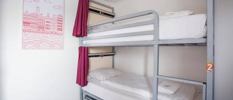 A bunk bed with two levels, each with a mattress and pillows. There is a poster on the wall depicting a cityscape.