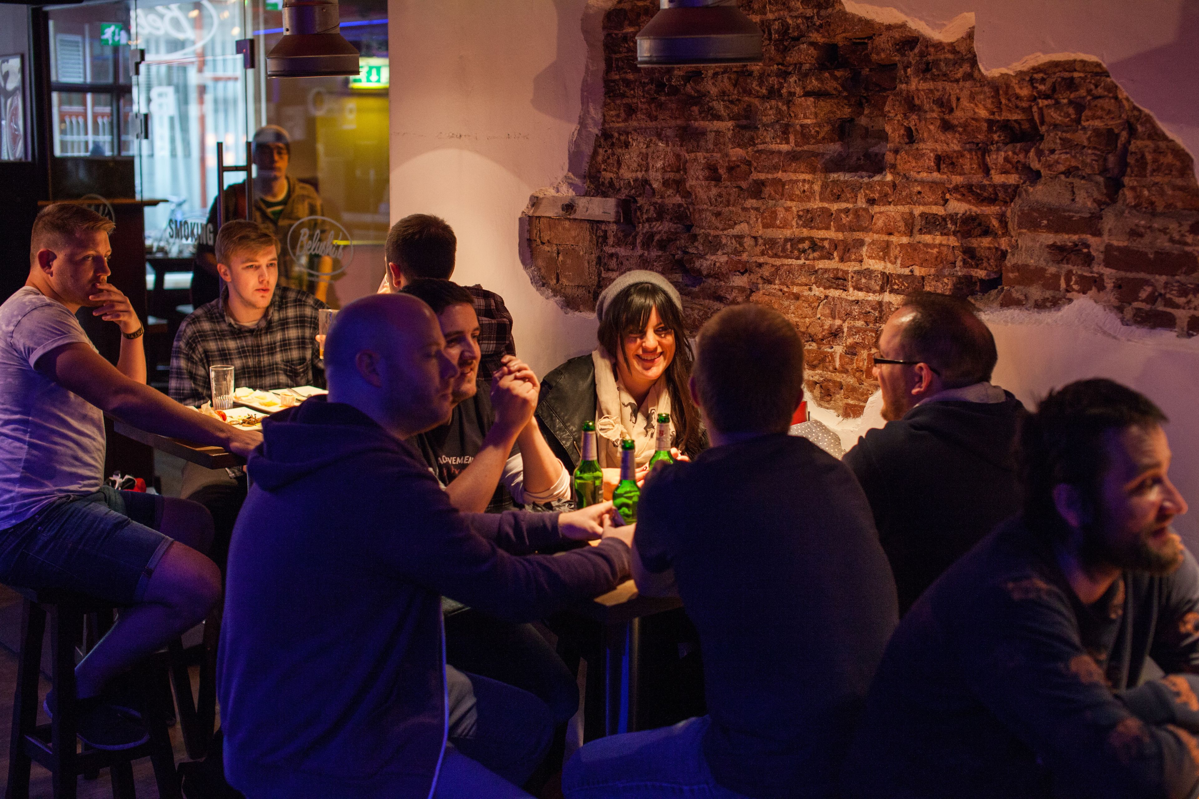 Un gruppo di persone sedute al bancone di un bar con un muro di mattoni sullo sfondo.