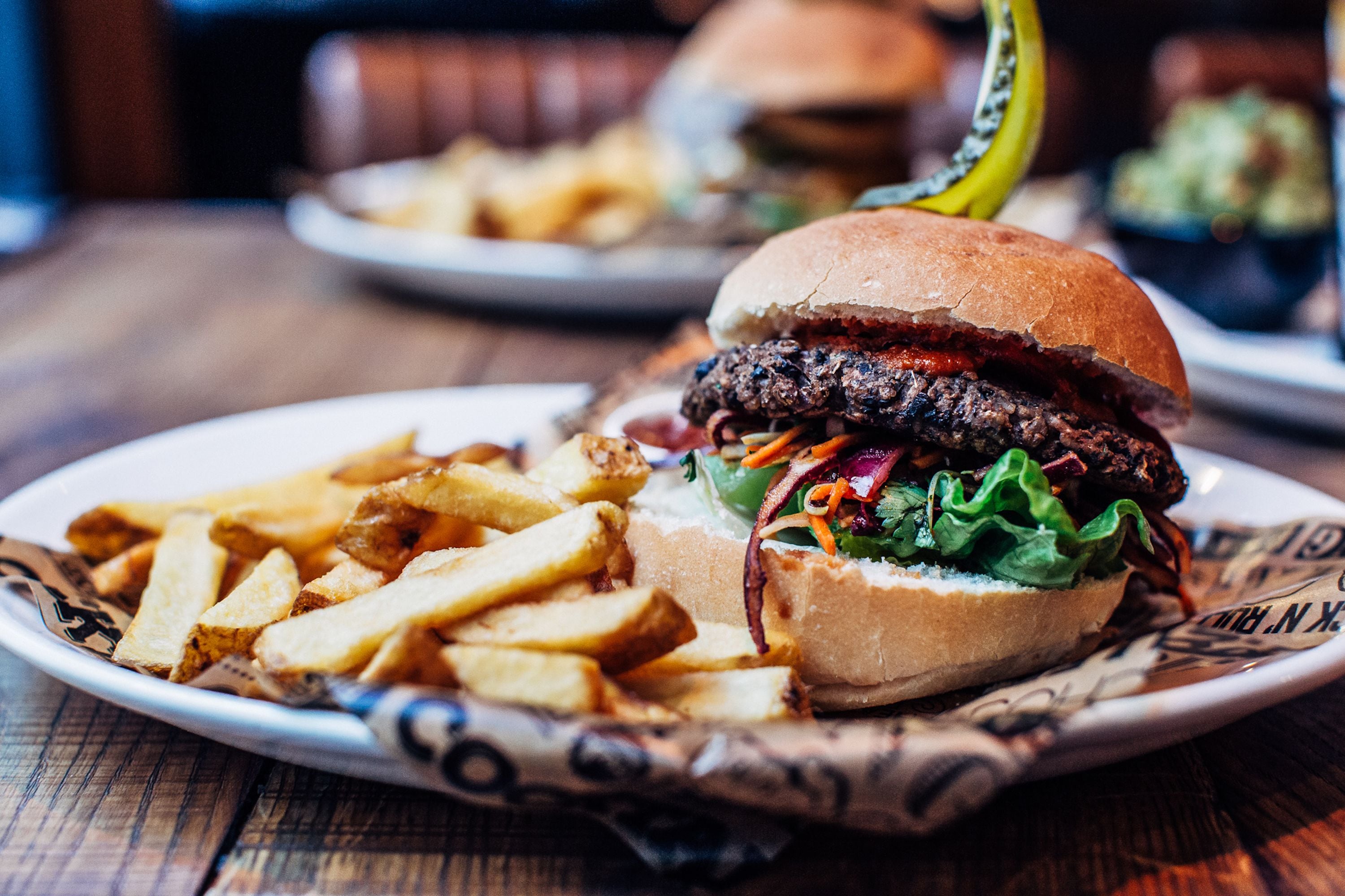 Um prato com um hambúrguer e batatas fritas sobre uma mesa de madeira.